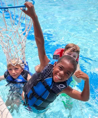 Three boys in lifejackets playing basketball in the pool