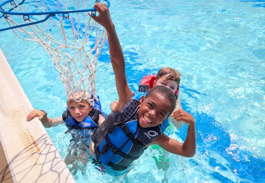 Three boys in lifejackets playing basketball in the pool